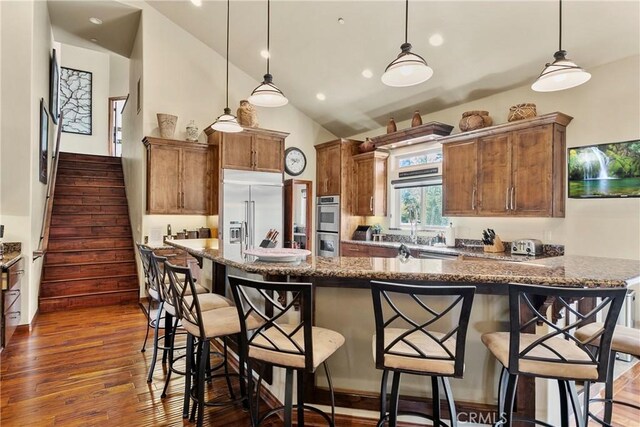 kitchen featuring vaulted ceiling, dark stone countertops, pendant lighting, a breakfast bar area, and stainless steel appliances