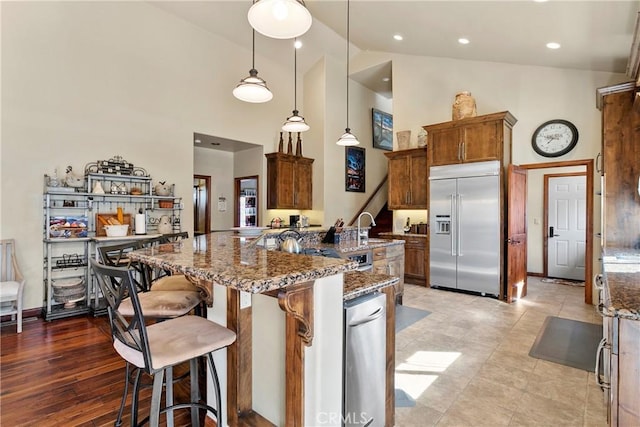 kitchen with decorative light fixtures, a kitchen breakfast bar, built in fridge, high vaulted ceiling, and light stone counters