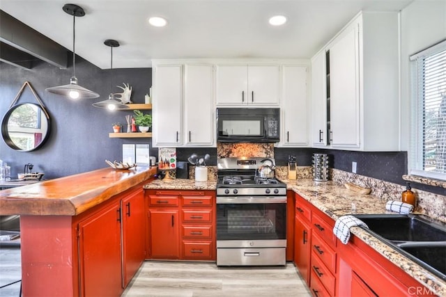 kitchen featuring gas range, decorative light fixtures, white cabinetry, and light hardwood / wood-style floors