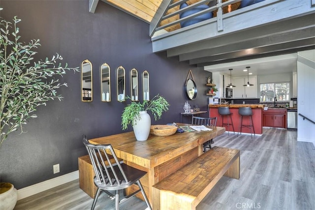 dining space with vaulted ceiling with beams, sink, and hardwood / wood-style flooring