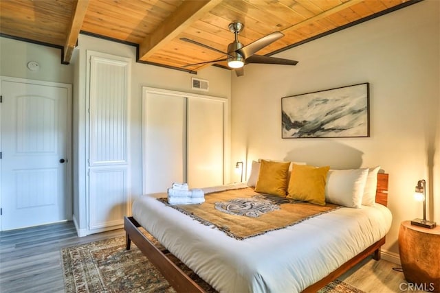 bedroom with beamed ceiling, hardwood / wood-style flooring, a closet, ceiling fan, and wooden ceiling