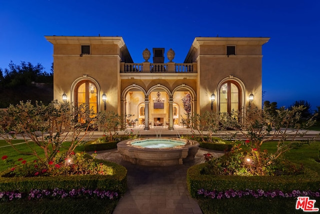 back house at night with a balcony and an in ground hot tub