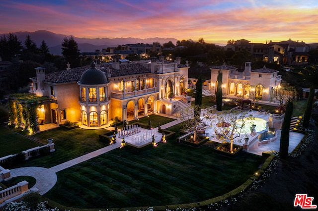 back house at dusk with a patio area, a lawn, and a pool