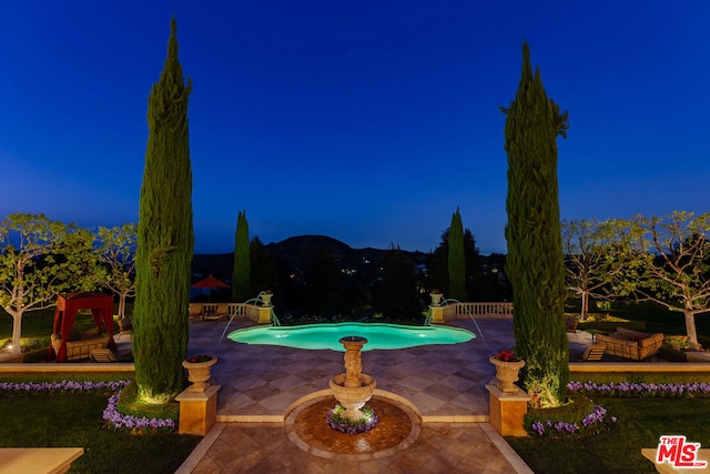 pool at night featuring a patio area and pool water feature