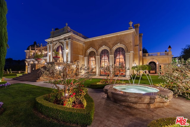 back house at night featuring an in ground hot tub and pool water feature