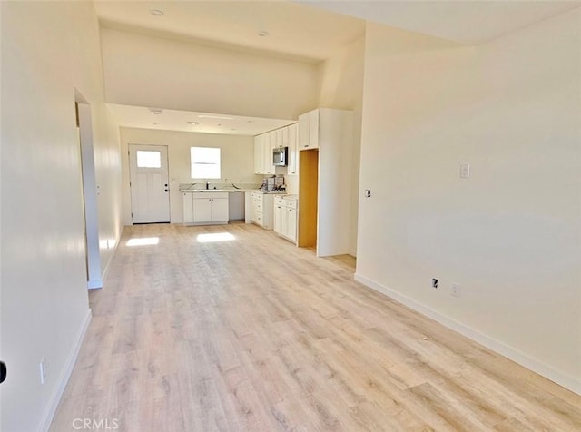 interior space with sink, high vaulted ceiling, white cabinetry, and light wood-type flooring