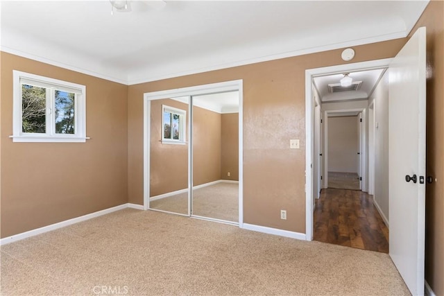 unfurnished bedroom featuring visible vents, ornamental molding, a closet, carpet flooring, and baseboards