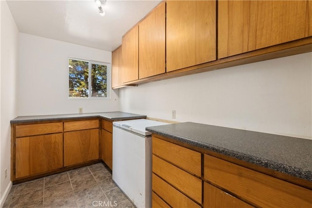 kitchen with fridge, dark countertops, and brown cabinetry