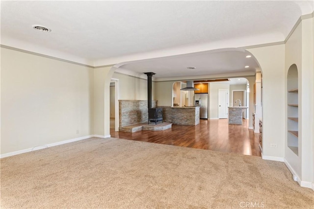 unfurnished living room with visible vents, baseboards, carpet floors, a wood stove, and arched walkways