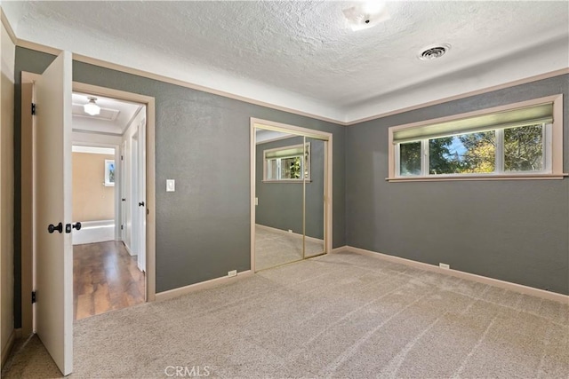 unfurnished bedroom with visible vents, a textured ceiling, a closet, carpet floors, and a textured wall