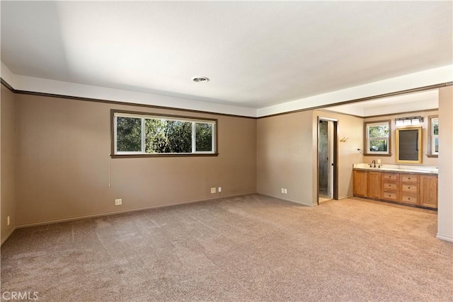 unfurnished bedroom featuring light colored carpet, visible vents, ensuite bathroom, and a sink