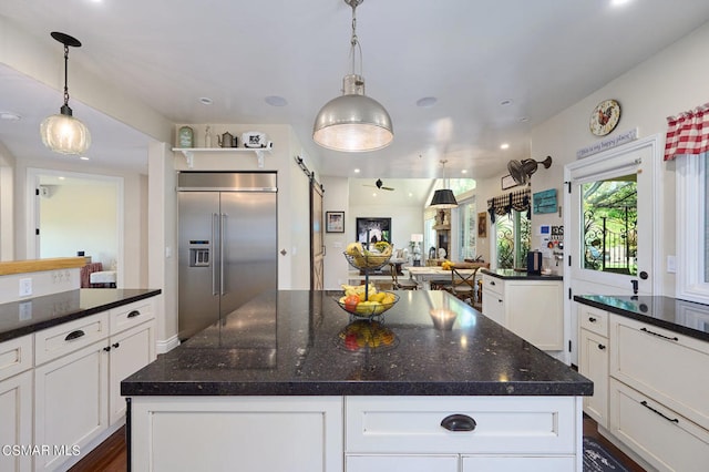 kitchen with white cabinets, a barn door, decorative light fixtures, a kitchen island, and stainless steel built in refrigerator