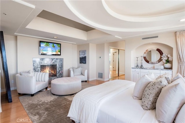 bedroom featuring a raised ceiling, a high end fireplace, and light hardwood / wood-style flooring