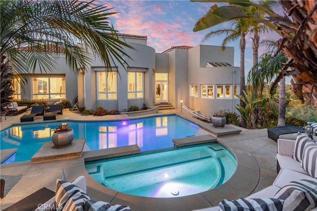 pool at dusk with an in ground hot tub, an outdoor hangout area, and a patio area