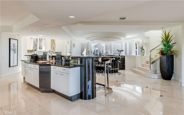 kitchen with a spacious island, a tray ceiling, a kitchen breakfast bar, and white cabinets