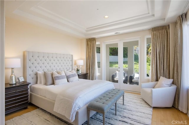 bedroom with access to exterior, a tray ceiling, light hardwood / wood-style flooring, and french doors