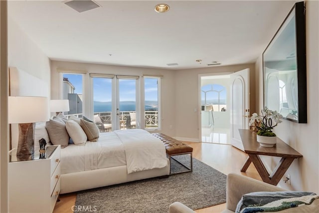 bedroom featuring a water view, access to exterior, and light hardwood / wood-style floors