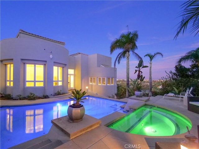 pool at dusk with an in ground hot tub and a patio