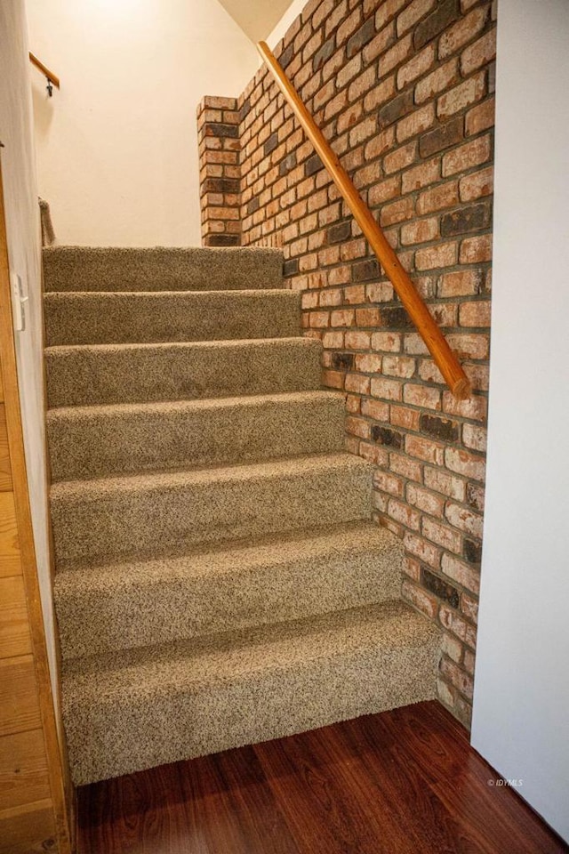 stairs with brick wall and hardwood / wood-style flooring