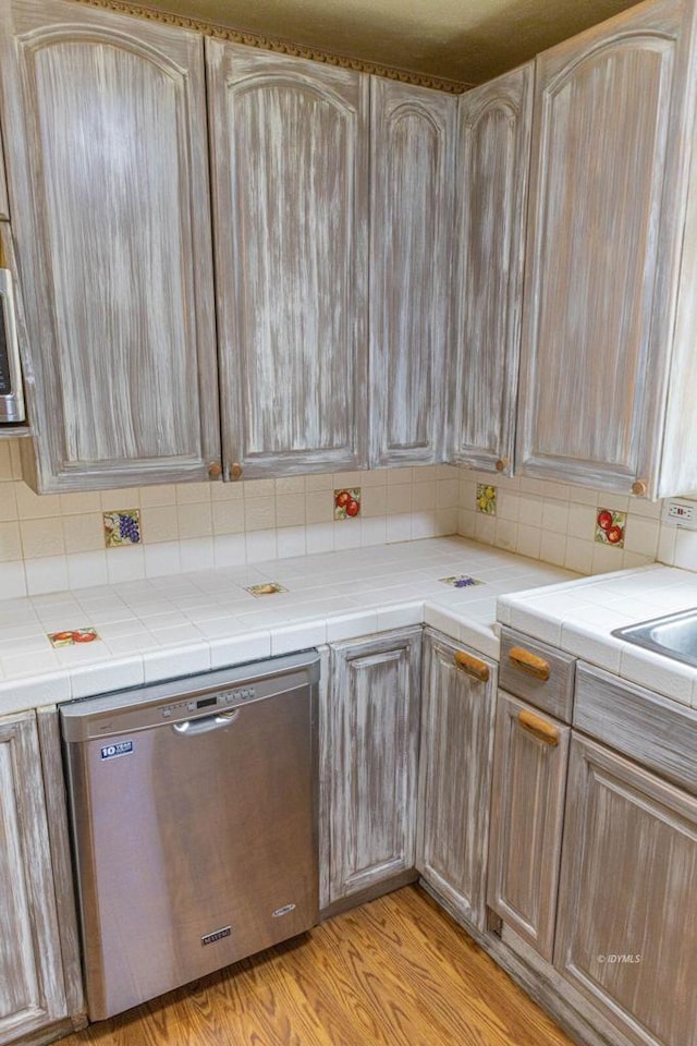 kitchen with light brown cabinetry, tile counters, dishwasher, and light hardwood / wood-style floors