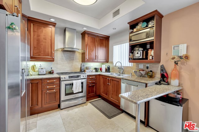 kitchen with light stone countertops, backsplash, sink, stainless steel appliances, and wall chimney range hood