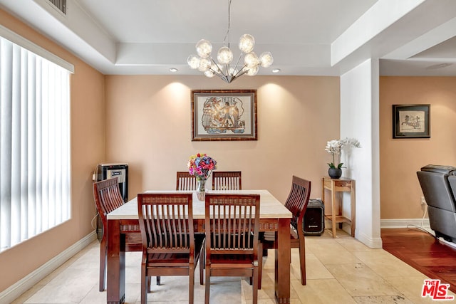 dining room with light hardwood / wood-style flooring, a notable chandelier, a raised ceiling, and a healthy amount of sunlight