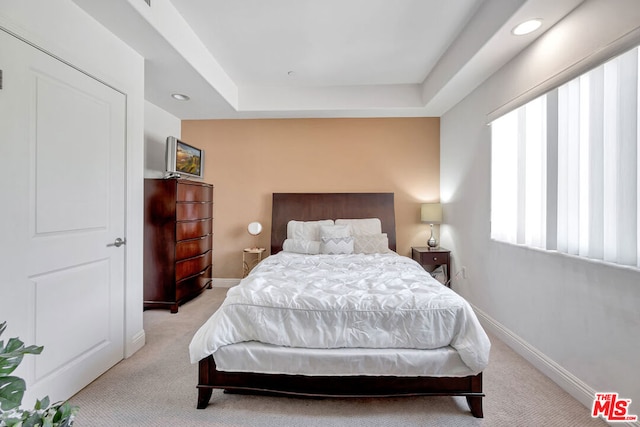 bedroom with a raised ceiling and light colored carpet