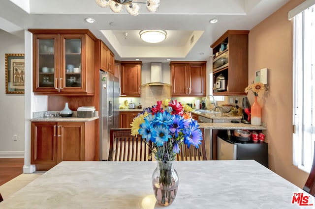 kitchen with light wood-type flooring, a tray ceiling, plenty of natural light, and wall chimney exhaust hood