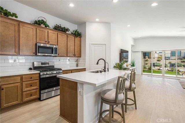 kitchen with sink, stainless steel appliances, a kitchen breakfast bar, a center island with sink, and light wood-type flooring