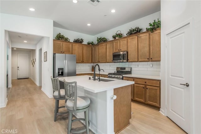 kitchen with a kitchen breakfast bar, light wood-type flooring, stainless steel appliances, a kitchen island with sink, and sink