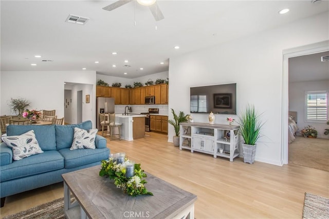 living room with ceiling fan, vaulted ceiling, sink, and light hardwood / wood-style flooring