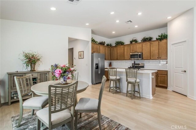 kitchen featuring backsplash, a kitchen island with sink, light wood-type flooring, appliances with stainless steel finishes, and a breakfast bar area