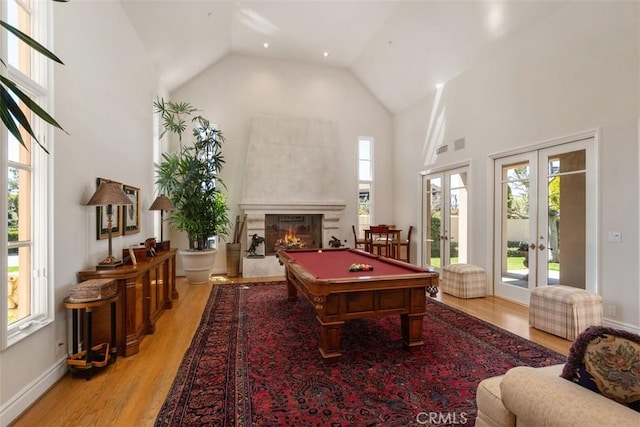 playroom featuring baseboards, a glass covered fireplace, light wood-style flooring, french doors, and high vaulted ceiling