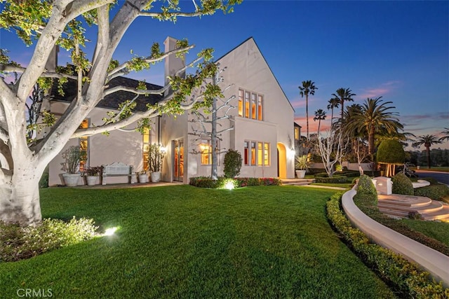 rear view of property with a chimney, a lawn, and stucco siding