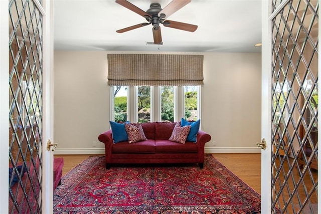 living room with a ceiling fan, visible vents, baseboards, and wood finished floors