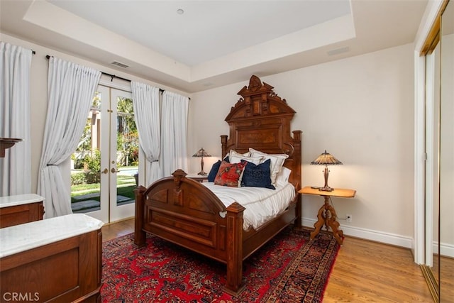 bedroom featuring access to exterior, baseboards, a tray ceiling, and light wood-style floors