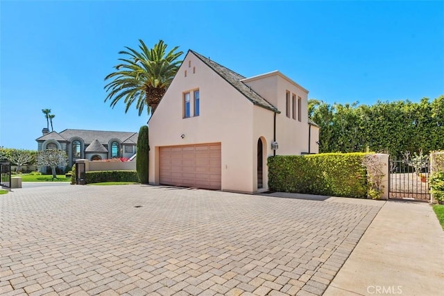 view of home's exterior with an attached garage, fence, decorative driveway, a gate, and stucco siding