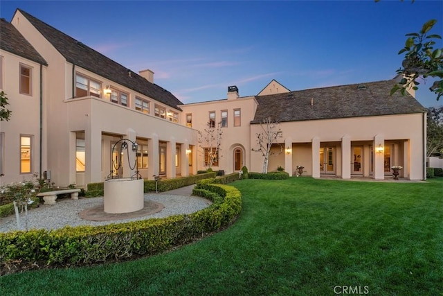 back of property at dusk featuring a lawn and stucco siding