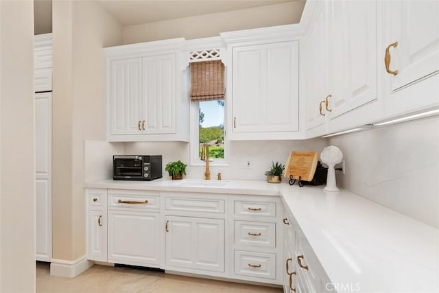 kitchen featuring light countertops, white cabinets, a toaster, and a sink