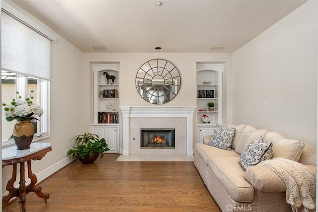 living room featuring baseboards, wood finished floors, a high end fireplace, and built in features