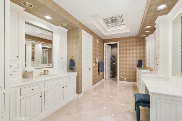 full bath with baseboards, two vanities, a sink, and wallpapered walls