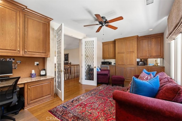 interior space with ceiling fan, french doors, built in desk, and light wood-style floors