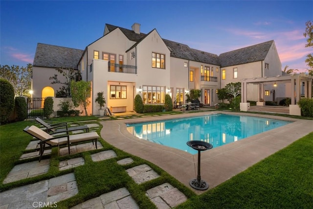 back of property with stucco siding, a patio area, fence, a balcony, and an outdoor pool