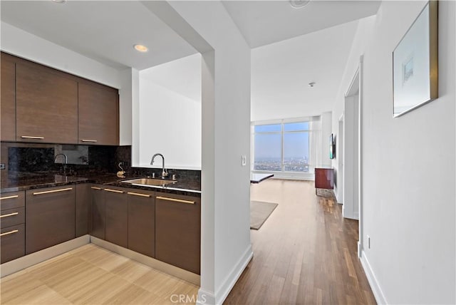 kitchen featuring decorative backsplash, dark brown cabinets, sink, light hardwood / wood-style flooring, and dark stone countertops