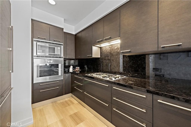 kitchen with appliances with stainless steel finishes, backsplash, dark brown cabinets, and dark stone counters