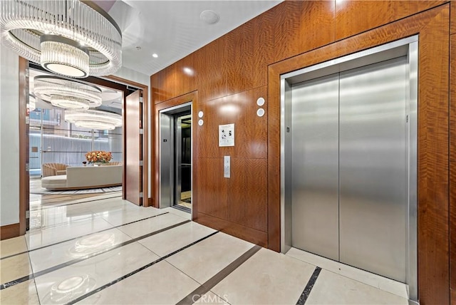 hall with a chandelier, elevator, and wooden walls