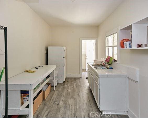 kitchen with tile countertops, light wood-style floors, freestanding refrigerator, white cabinetry, and a sink