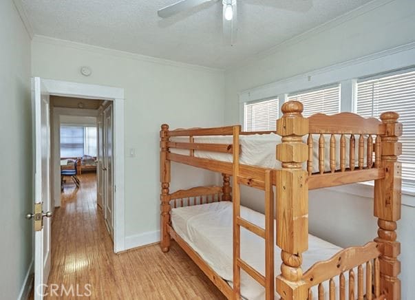 bedroom featuring multiple windows, ornamental molding, ceiling fan, and light wood-type flooring