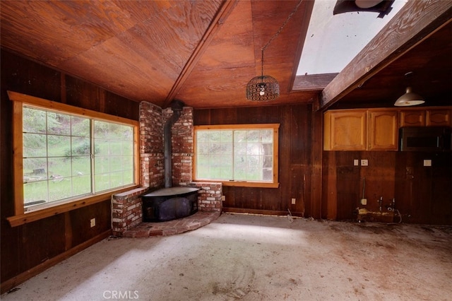 unfurnished living room featuring wood walls, plenty of natural light, and a wood stove