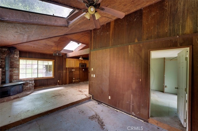 unfurnished living room featuring ceiling fan, vaulted ceiling with skylight, a wood stove, brick wall, and wood walls